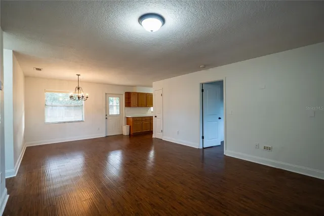 an empty room with wooden floor kitchen and windows