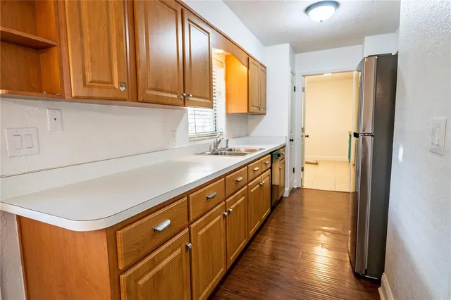 a kitchen with stainless steel appliances granite countertop a refrigerator a sink dishwasher and wooden cabinets with wooden floor