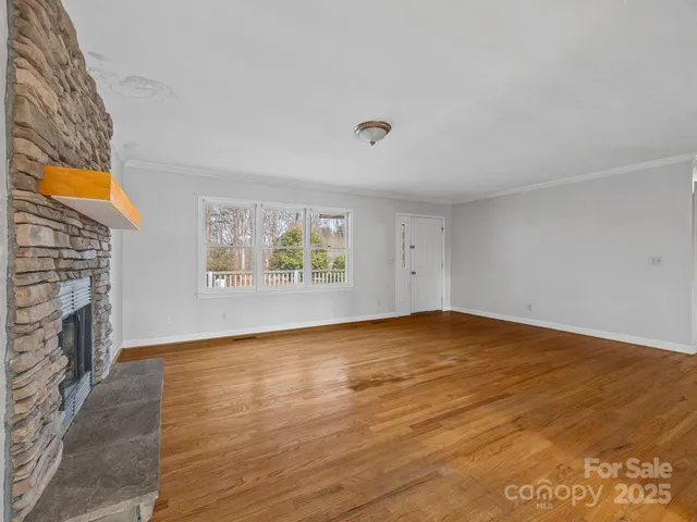 a view of an empty room with wooden floor and a fireplace