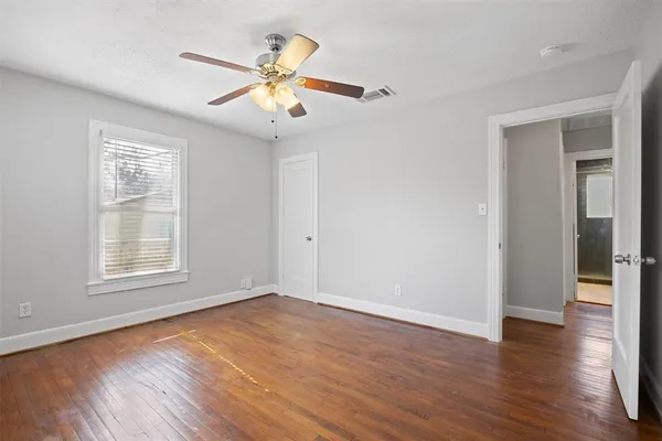 an empty room with wooden floor fan and windows