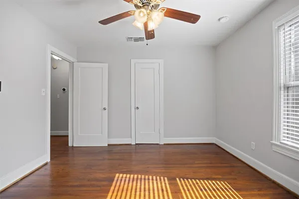 an empty room with wooden floor chandelier fan and windows