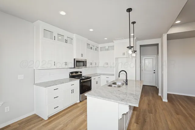 a kitchen with stainless steel appliances a sink a stove a refrigerator and white cabinets with wooden floor