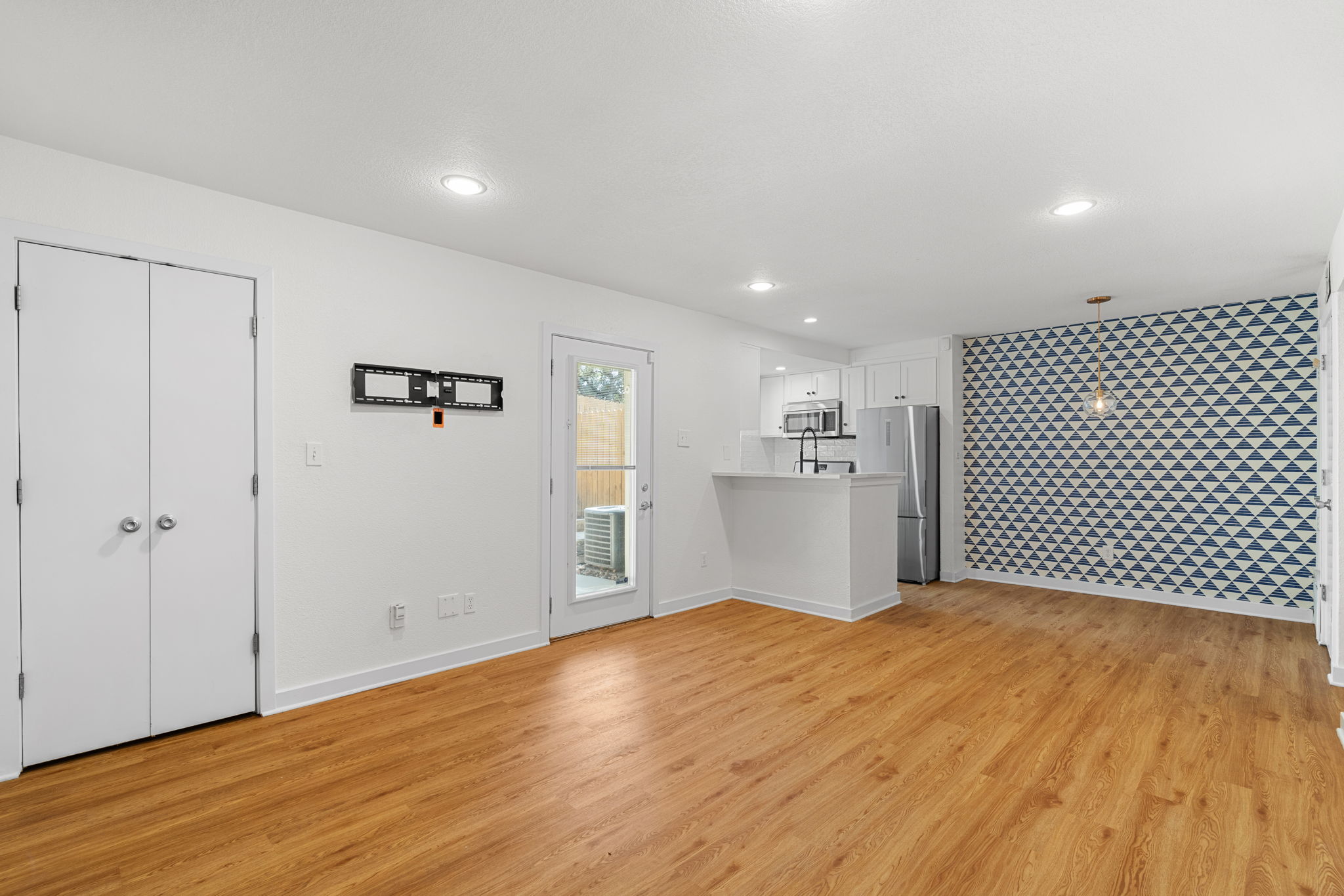 3601 Menchaca Road, Unit 110 Austin, TX 78704 - Photo 6 of 37 A well-lit open-concept living area with gleaming hardwood flooring flows seamlessly into a modern kitchen, anchored by a captivating geometric accent wall.