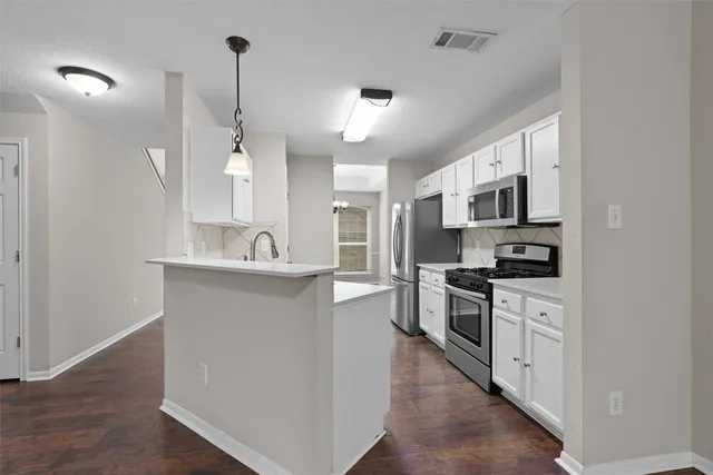 a large kitchen with stainless steel appliances granite countertop a stove top oven a sink dishwasher and a refrigerator with wooden floor