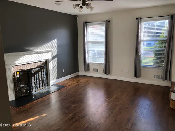 an empty room with wooden floor fireplace and windows