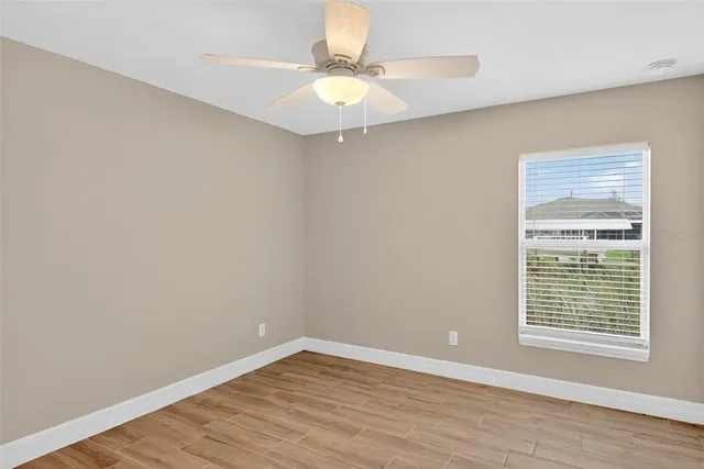 an empty room with wooden floor chandelier fan and windows