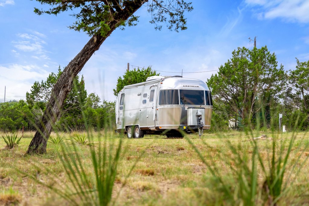 2126 Hidden Valley Ranch Road Johnson City, TX 78636 - Photo 30 of 36 A sleek Airstream trailer rests amidst a verdant landscape under a bright sky.