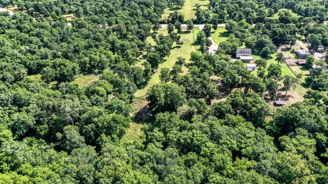 an aerial view of residential house with outdoor space and trees all around