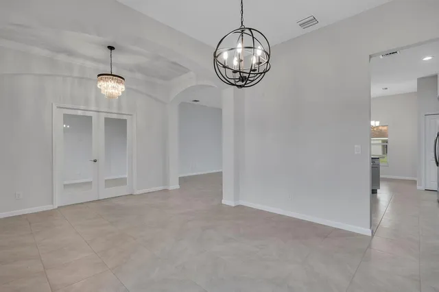 an empty room with chandelier fan and kitchen view