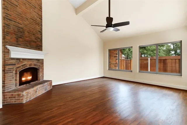 a view of a livingroom with wooden floor a fireplace a ceiling fan and window