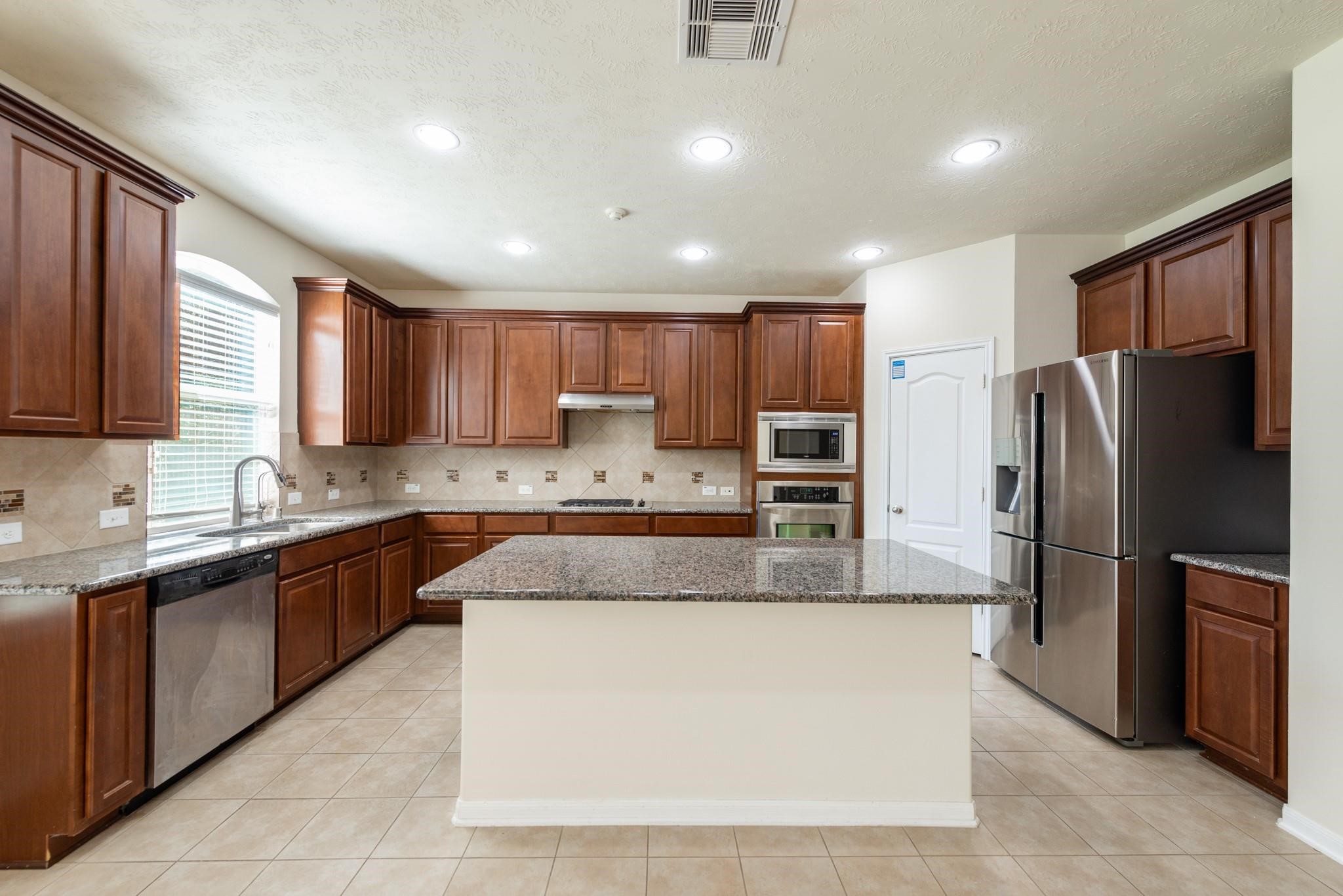 6402 Addlestone Ridge Lane Katy, TX 77494 - Photo 7 of 25 View from the family room showcasing the impressive kitchen with its oversized granite island, extensive cabinetry, stainless steel appliances, built-in microwave and oven, gas cooktop, and walk-in pantry. The open-concept design keeps everyone connected whether cooking, dining, or entertaining.
