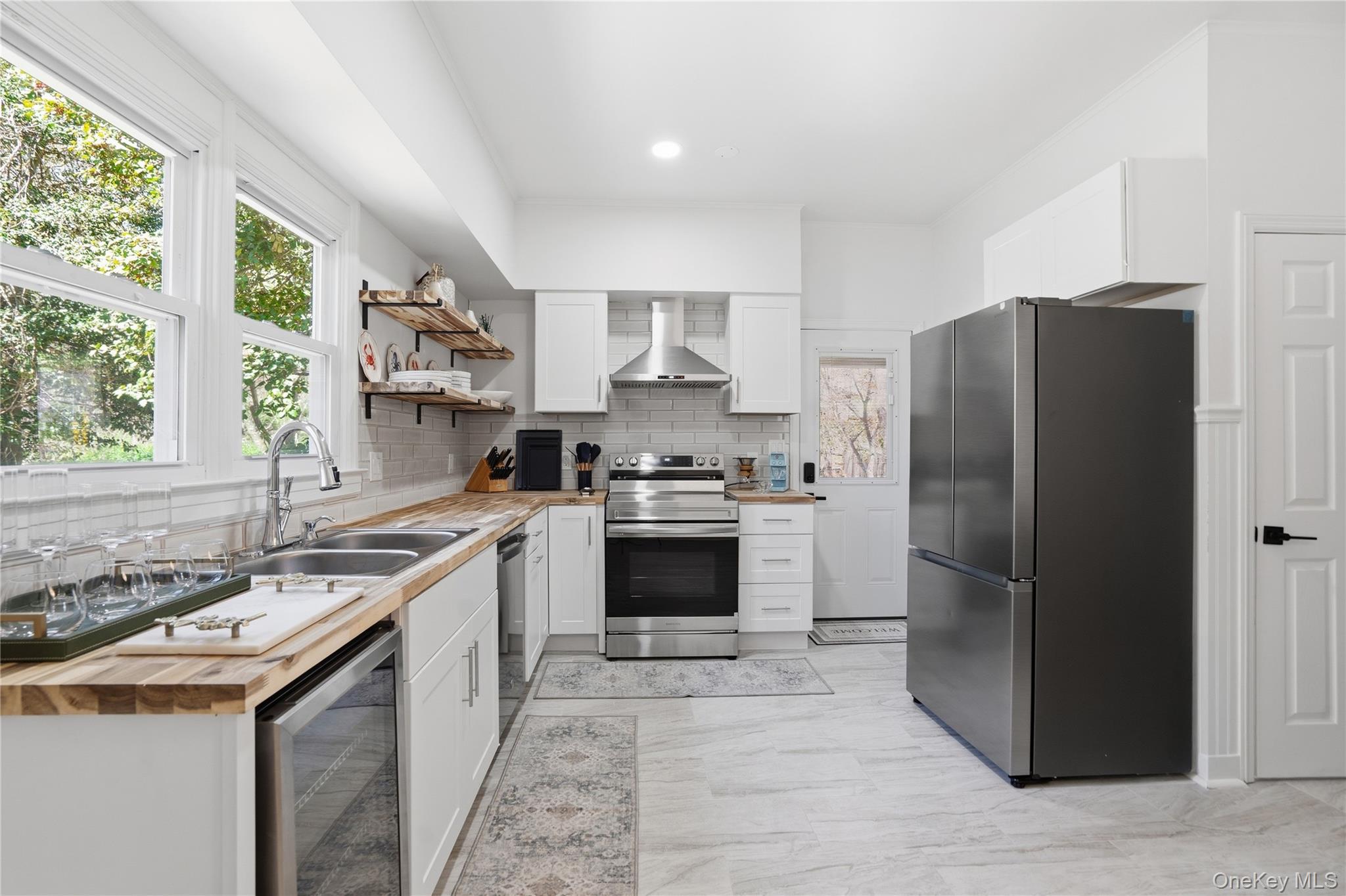 1550 Main Road Riverhead, NY 11901 - Photo 7 of 28 Modern kitchen featuring stainless steel appliances, white cabinetry, wood-finish countertops, open shelving, and a tile backsplash