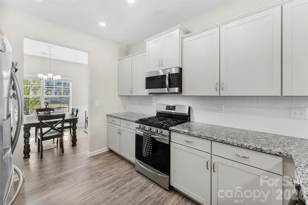a kitchen with stainless steel appliances granite countertop a stove top oven a sink and white cabinets