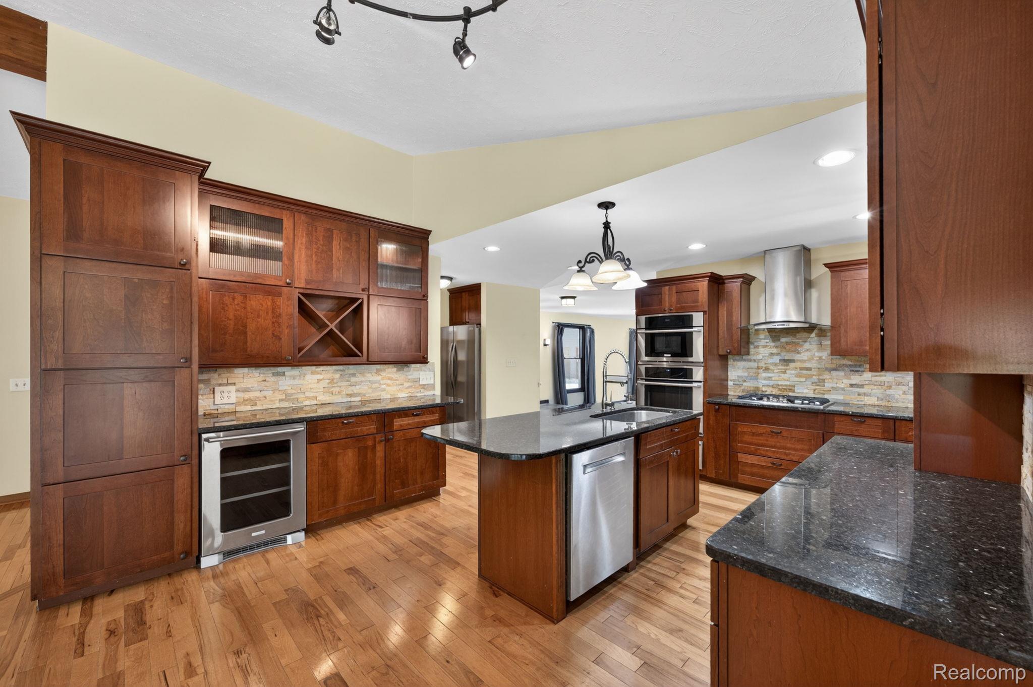 9353 Hill Road Swartz Creek, MI 48473 - Photo 25 of 98 Gourmet kitchen featuring hardwood flooring, dark wood cabinetry, granite countertops, a stone tile backsplash, and stainless steel appliances including a built-in wine cooler