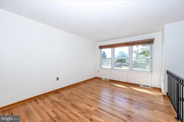 a view of an empty room with wooden floor and fan