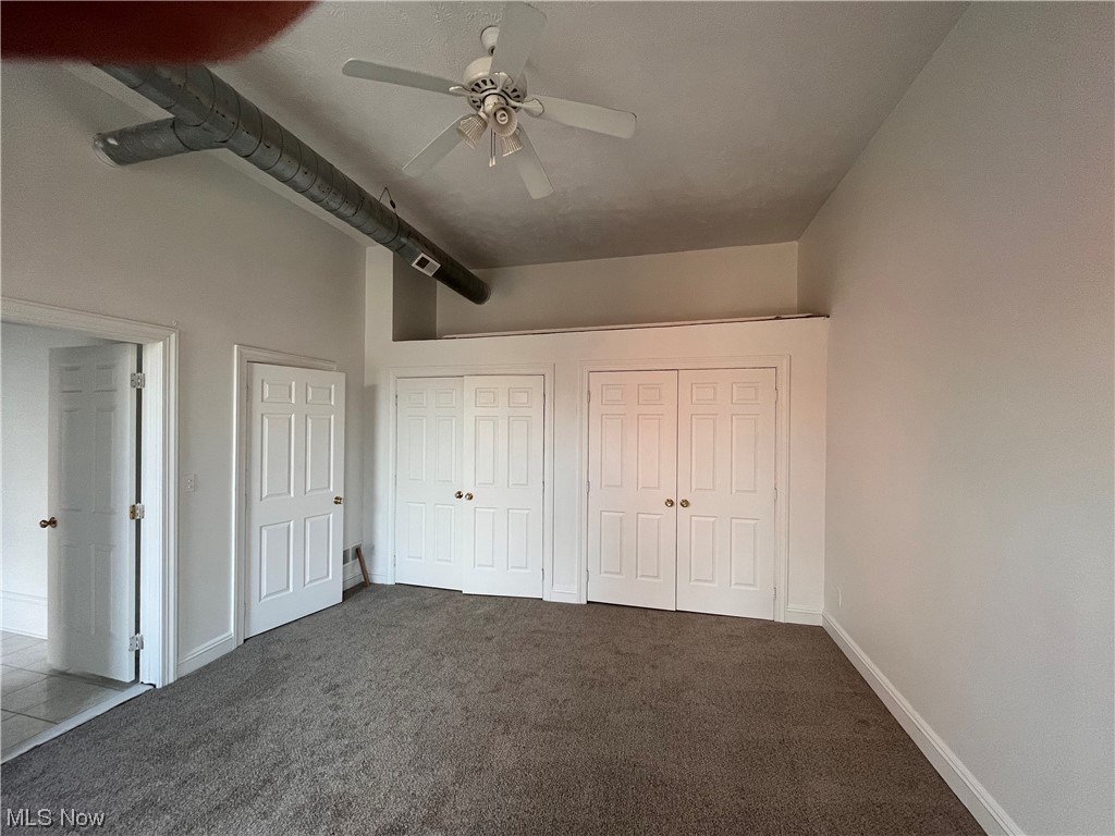 1697 Fulton Road Cleveland, OH 44113 - Photo 17 of 23 Unfurnished bedroom featuring two closets, dark colored carpet, beam ceiling, and ceiling fan