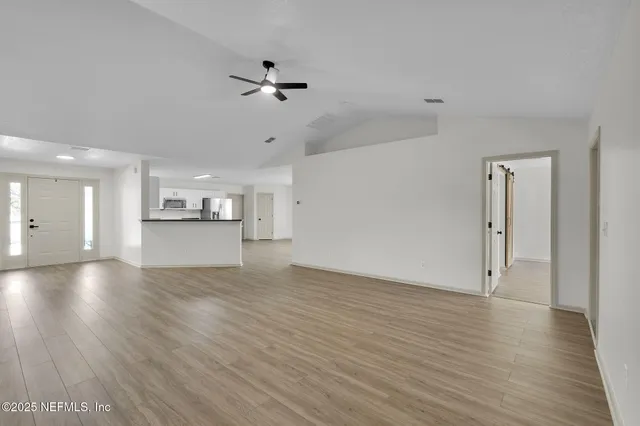 a view of empty room with wooden floor and a kitchen