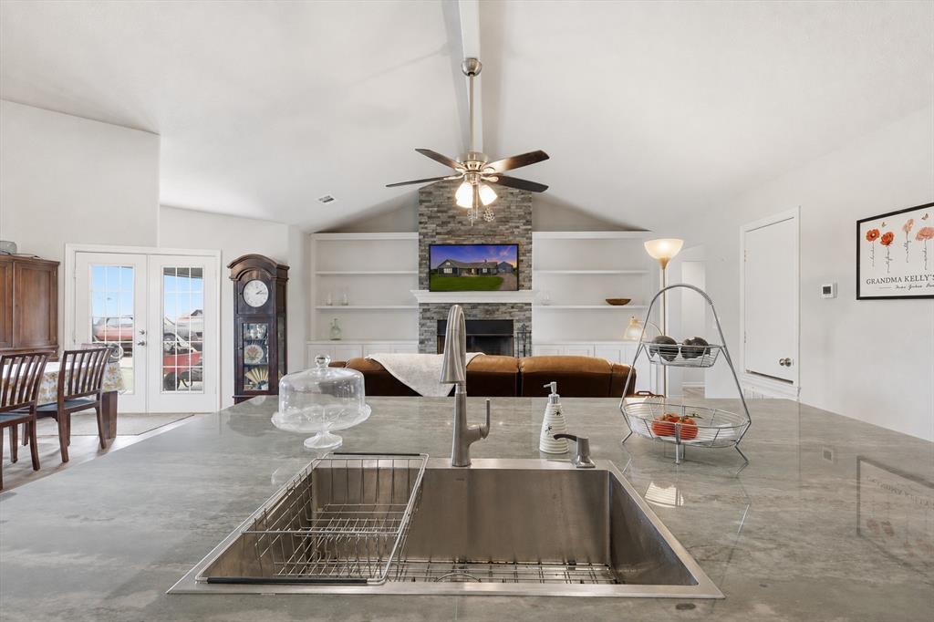 Virtually Enhanced -Kitchen island with an undermount sink, a vaulted ceiling, a ceiling fan, a stone-clad fireplace, and built-in shelving