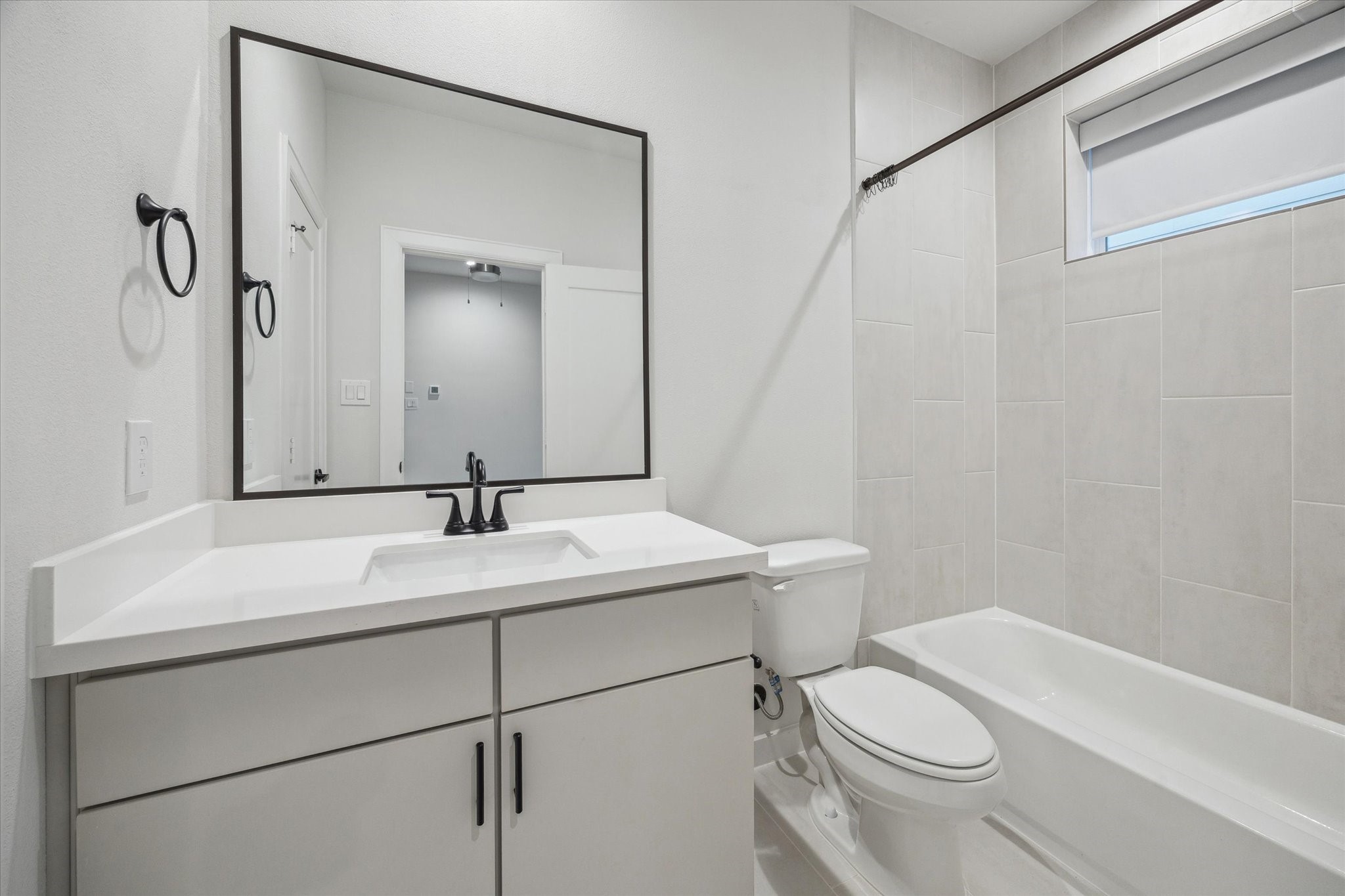 1603 Patterson Street, Unit E Houston, TX 77007 - Photo 30 of 32 This bathroom features a modern design with a sleek white vanity, black fixtures, and a large mirror. The space includes a bathtub with tiled walls and a window for natural light, creating a bright and clean atmosphere.