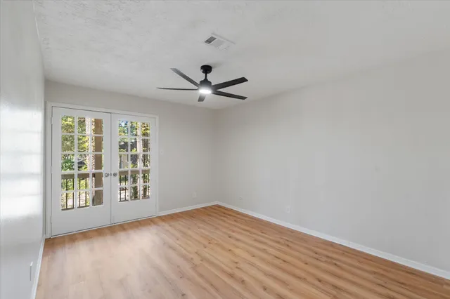an empty room with wooden floor fan and windows