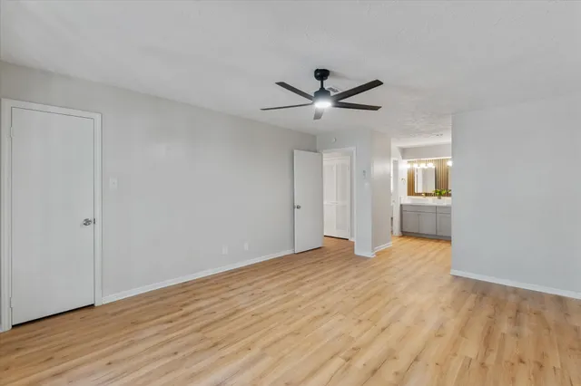 a view of an empty room with wooden floor and a ceiling fan