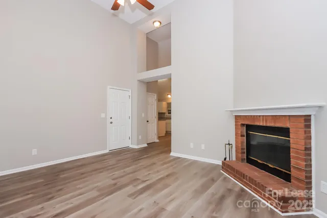 a view of an empty room with wooden floor a fireplace and a window