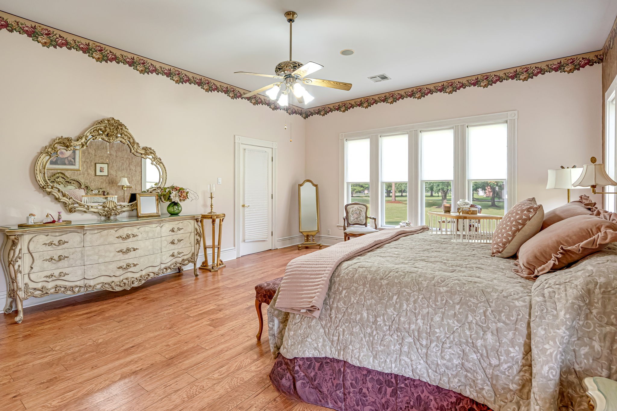 4028 Crosby Cedar Bayou Road Baytown, TX 77521 - Photo 21 of 35 From the en-suite entrance, the primary bedroom unfolds as a true retreat—hardwood floors, high ceilings with a ceiling fan, and a generous wall of windows that frame serene views. A convenient door leads directly to the sunroom, extending the suite with bright, year-round living space.