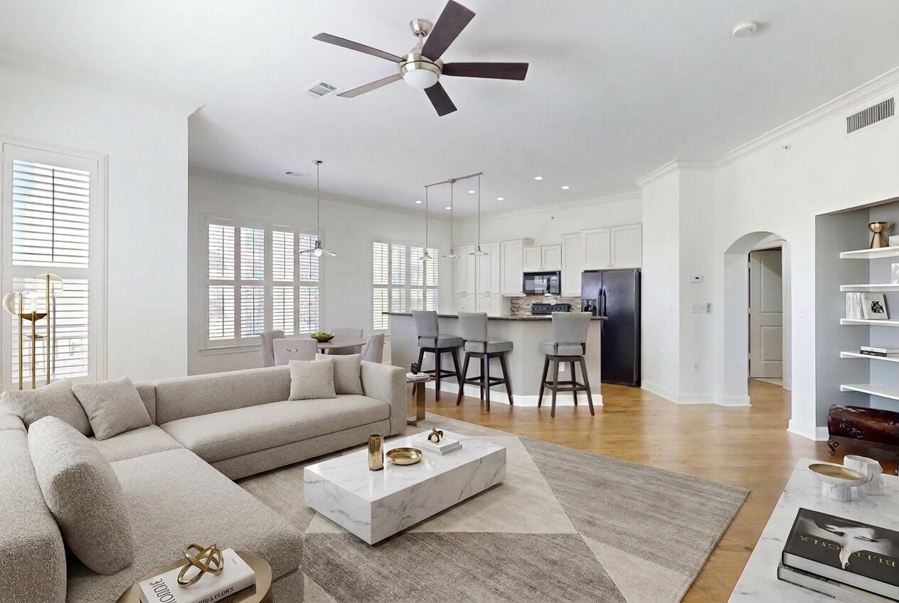 1010 Rosine Street, Unit 29 Houston, TX 77019 - Photo 15 of 16 This spacious, modern living area features an open floor plan with a cozy sectional sofa, a sleek marble coffee table, and abundant natural light from large windows. The adjacent kitchen boasts white cabinetry, stainless steel appliances, and a breakfast bar with stylish stools, perfect for entertaining. (Virtual Staging)