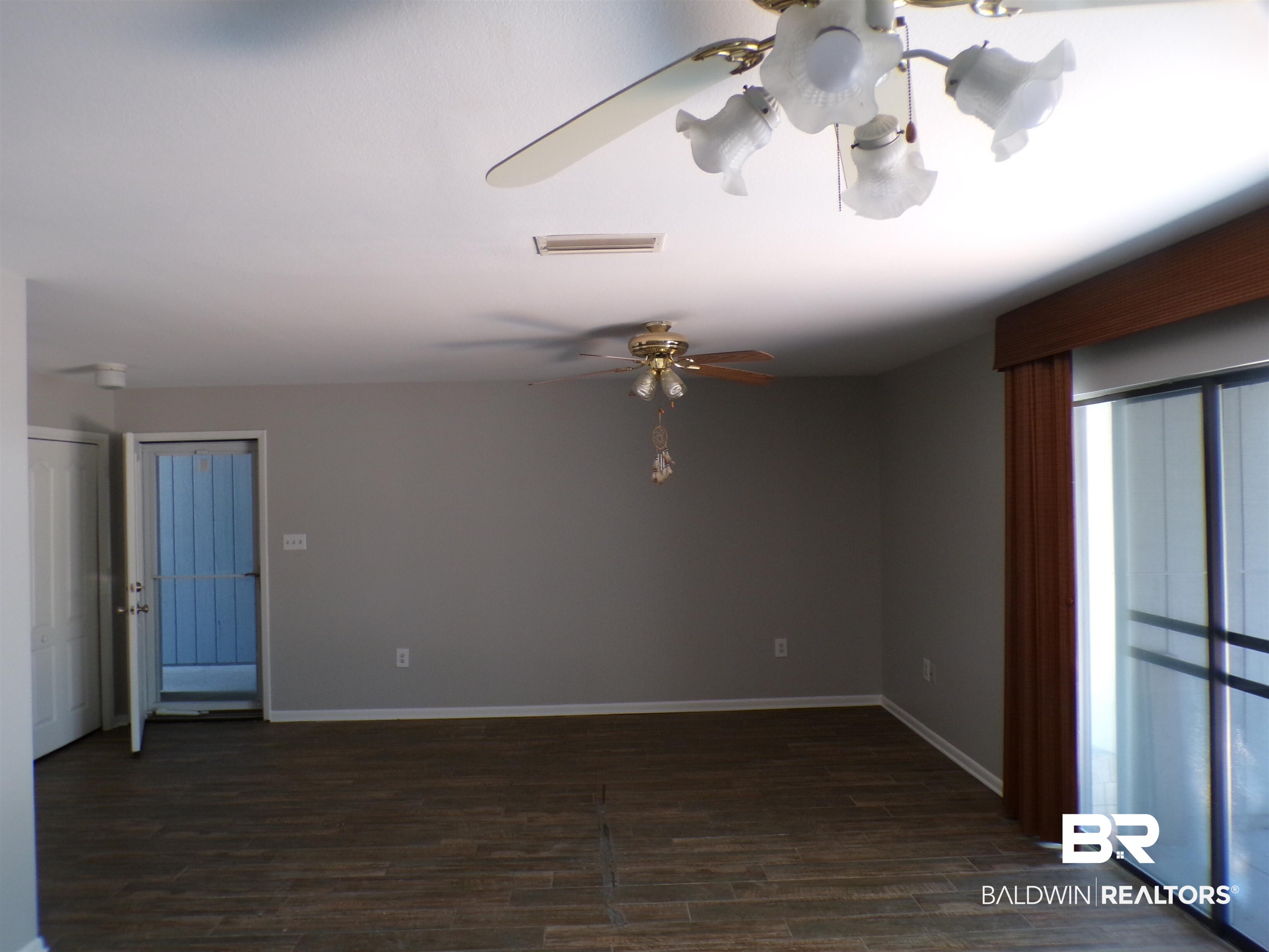 1152 North Alston Street, Unit 1152 Foley, AL 36535 - Photo 4 of 16 Spacious room featuring wood-finish flooring, light grey walls, and a large sliding glass door with vertical blinds