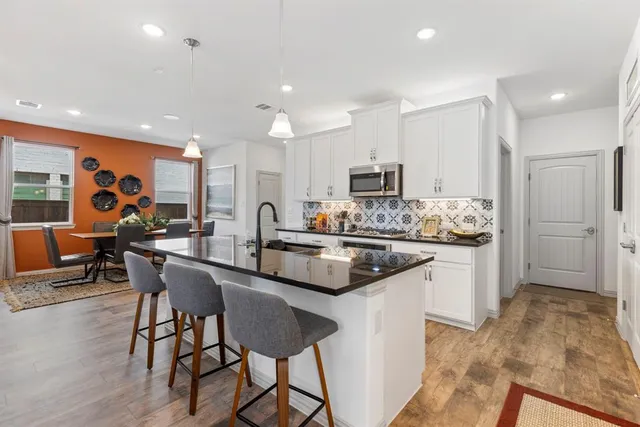 a kitchen with stainless steel appliances a sink a stove a refrigerator cabinets and chairs