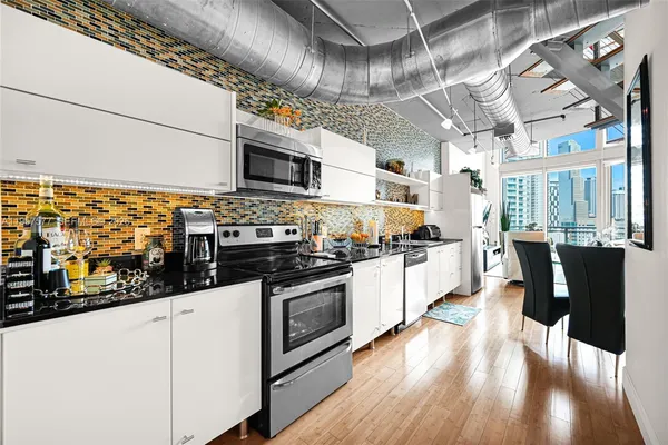 a kitchen with stainless steel appliances kitchen island granite countertop a refrigerator a stove and white cabinets with wooden floor