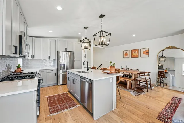a kitchen with stainless steel appliances granite countertop a stove oven a refrigerator a sink dishwasher a dining table and chairs with wooden floor