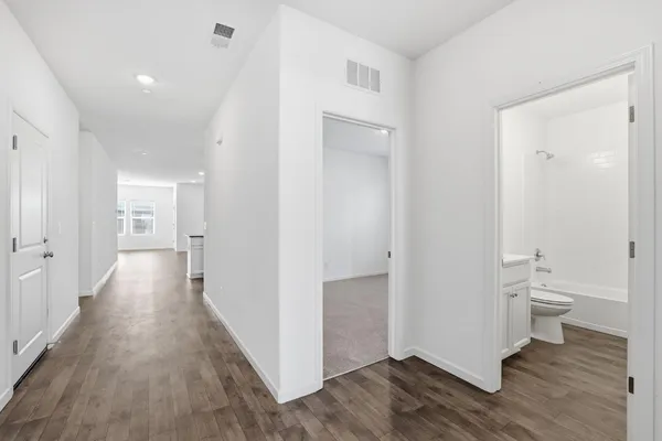 a view of a hallway with wooden floor and a bathroom