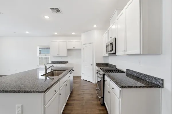 a kitchen with granite countertop kitchen island stainless steel appliances a sink a stove a refrigerator and blue cabinets
