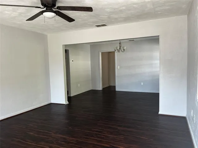 an empty room with wooden floor a ceiling fan and kitchen view