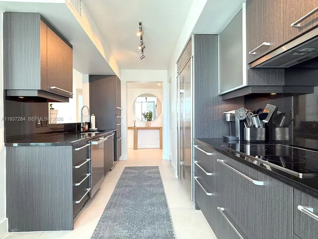 a kitchen with stainless steel appliances granite countertop a refrigerator a sink dishwasher a stove and a dining table with wooden floor