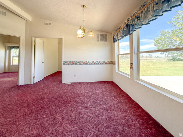 141 South 100 East Emery, UT 84522 - Photo 5 of 17 Bright interior space with deep red patterned carpeting, a three-light chandelier, and large windows revealing a verdant outdoor landscape