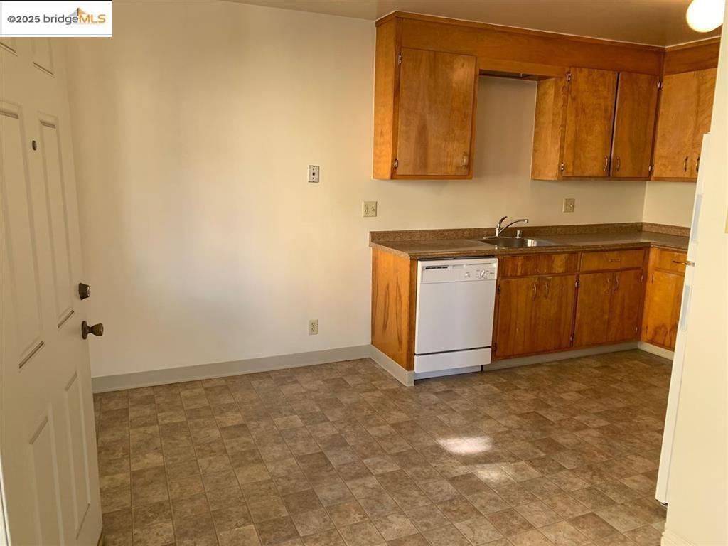708 Solano Avenue, Unit D Albany, CA 94706 - Photo 7 of 23 Kitchen featuring brown cabinets, dark countertops, white dishwasher, and stone finish floors