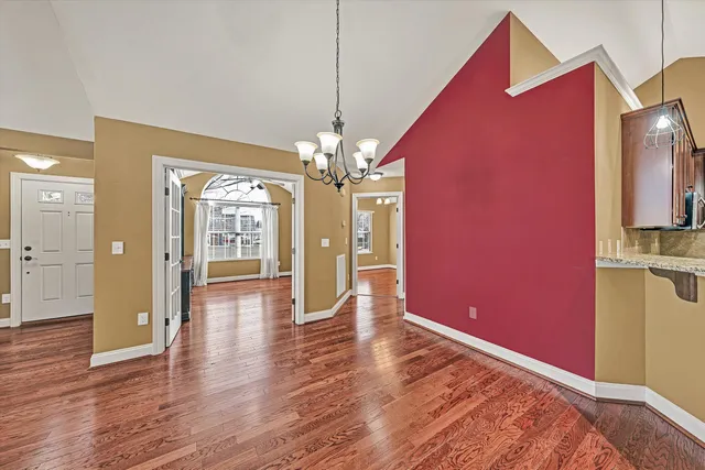 a view of an empty room with wooden floor and a kitchen