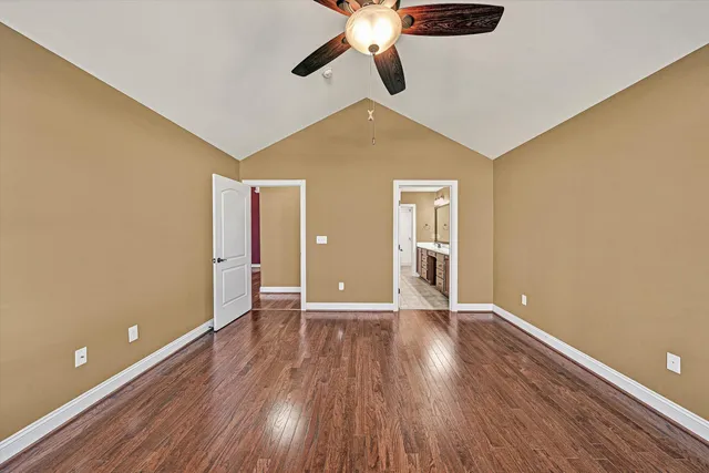 a view of an empty room with wooden floor and a ceiling fan