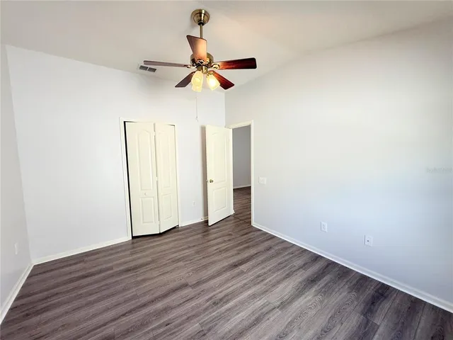 a view of a room with wooden floor closet ceiling fan and window