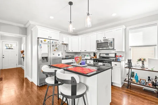 a kitchen with stainless steel appliances kitchen island granite countertop a refrigerator a stove top oven a sink dishwasher and a dining table with wooden floor