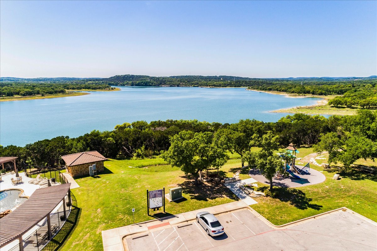 8008 Prairie Rye Drive Lago Vista, TX 78645 - Photo 34 of 40 Expansive lakefront setting featuring a terraced pool area, a stone-clad building with a tiled roof, a dedicated children's play structure, and mature trees on a grassy lawn