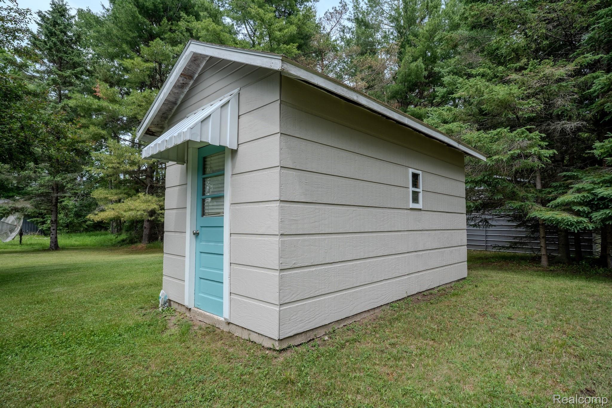4350 Shrew Road Lincoln, MI 48742 - Photo 29 of 32 Storage shed featuring light-colored siding, a pitched roof, and a turquoise-painted door with a white awning