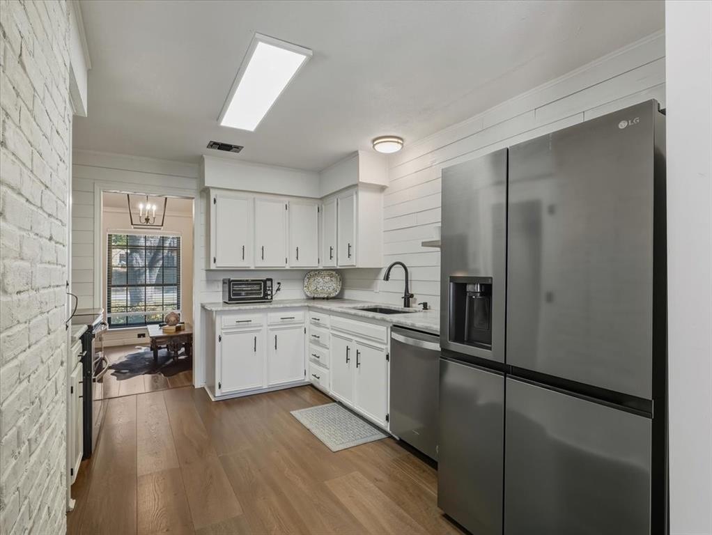 1662 Watson Road Fort Worth, TX 76103 - Photo 11 of 37 Kitchen featuring stainless steel appliances, white cabinetry, dark wood-type flooring, brick wall, and a chandelier