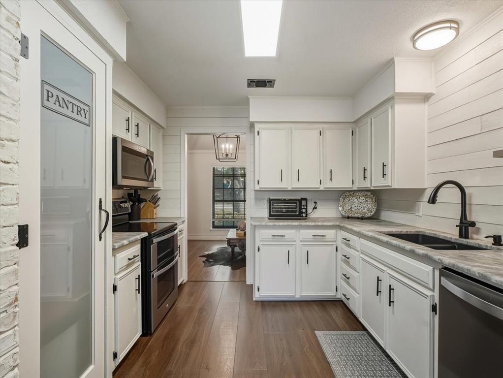 1662 Watson Road Fort Worth, TX 76103 - Photo 10 of 37 Kitchen featuring stainless steel appliances, white cabinets, dark wood-style floors, wood walls, and light stone counters