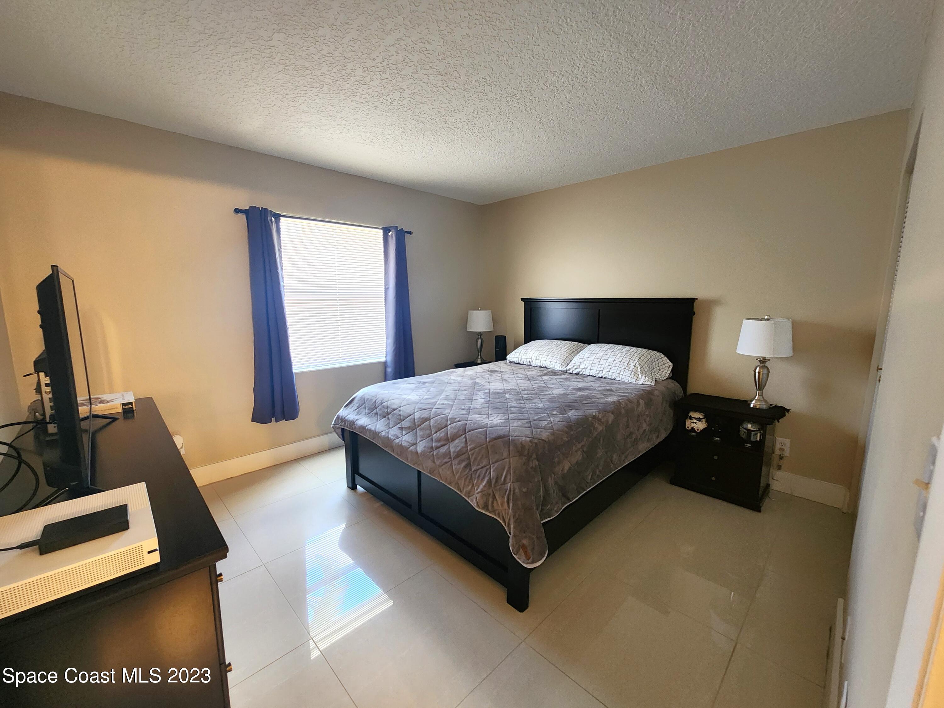 582 North Wickham Road, Unit 89 Melbourne, FL 32934 - Photo 14 of 25 a bedroom with a bed and a flat tv screen on the dresser