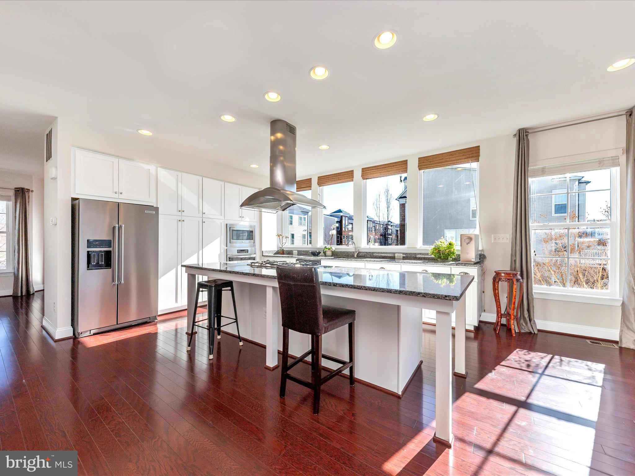 42251 Riggins Ridge Terrace Brambleton, VA 20148 - Photo 12 of 62 a kitchen with stainless steel appliances kitchen island granite countertop a table chairs refrigerator and sink