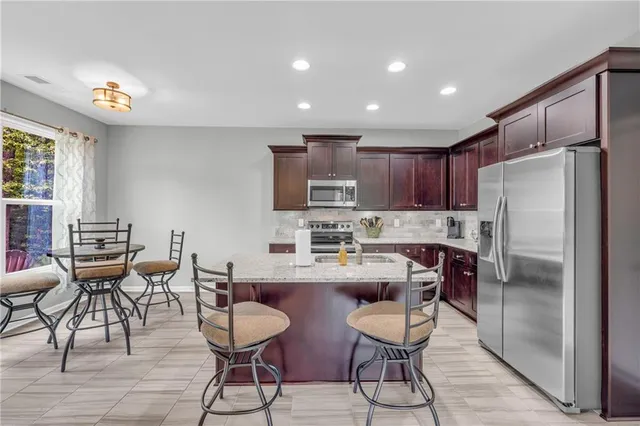 a kitchen with stainless steel appliances granite countertop a refrigerator a stove a sink a dining table and chairs with wooden floor