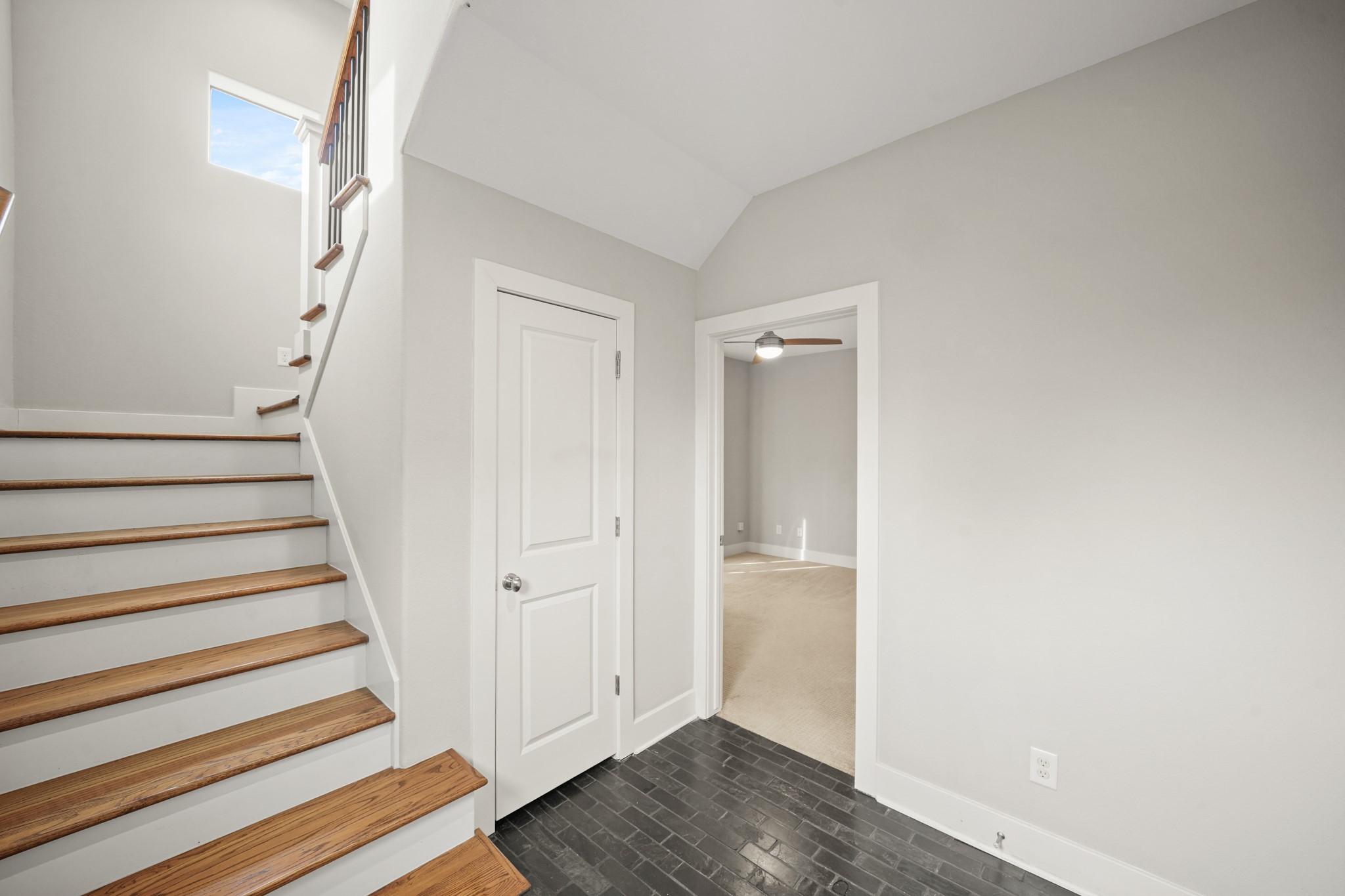 2547 Calumet Street Houston, TX 77004 - Photo 6 of 28 This photo showcases a bright entryway with hardwood stairs and a tile floor. It leads to a carpeted room with a ceiling fan, and there's a small window illuminating the staircase.